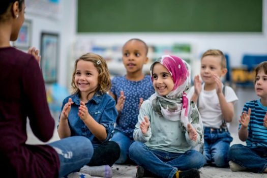 مجموعة من الأطفال تقوم يصفقون بأيديهم مع المعلمة التي تقوم بتشجيعهم